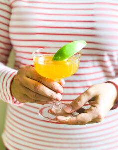 A bubbly apple cocktail in champagne coupe with green apple slice held in front of striped shirt