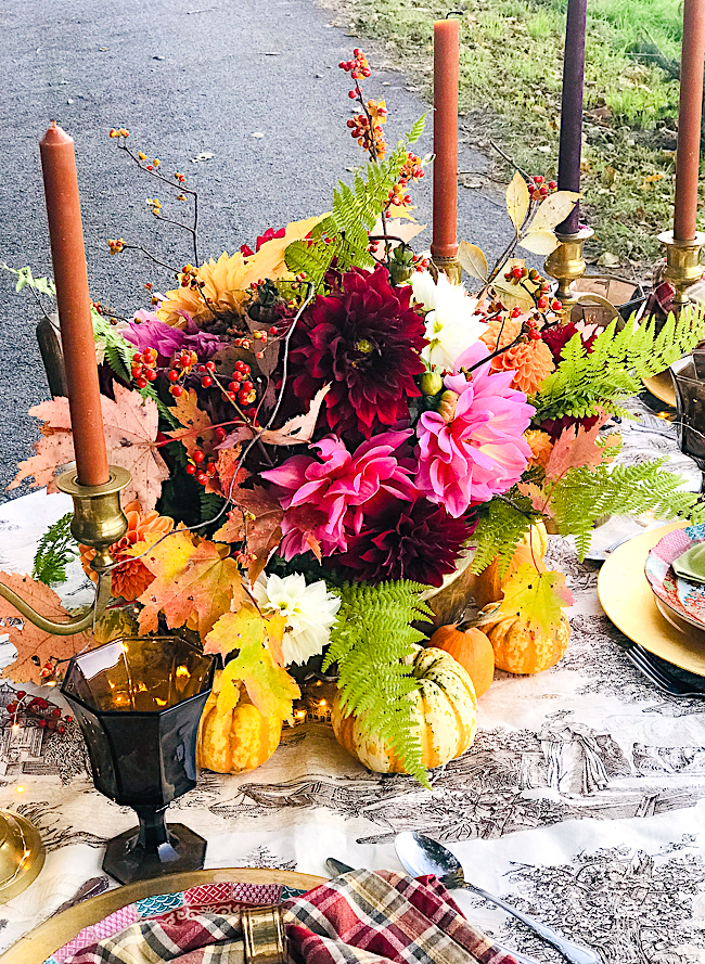 A riot of colorful dahlias, autumn foliage, bittersweet berries, and fern nestle in a brass bowl for this Thanksgiving table centerpiece.