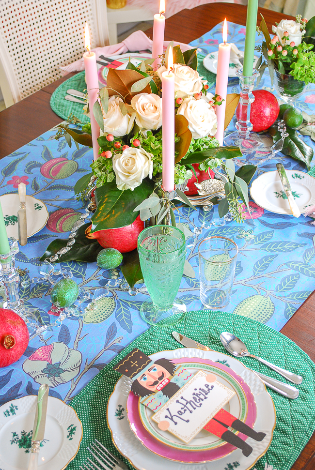 a bold Christmas tablescape set with a William Morris print, centerpiece of white roses and magnolia, polka dot placemats, and layered pink and green china