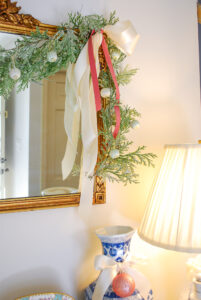 Glittery cedar garland with satin white and pink streamers draped over gold mirror