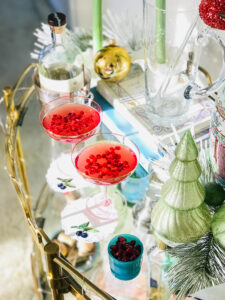 Two champagne coupes on a gold bar cart full of pomegranate gin holiday cocktails
