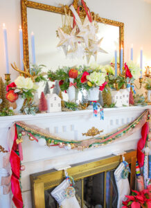 White amaryllis, hot pink ribbon, and greenery mixed with a white Christmas village make for a colorful and whimsical holiday mantel