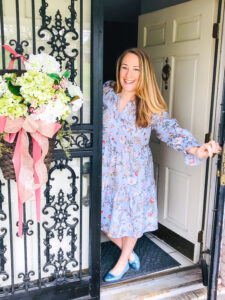 Katherine in Gal Meets Glam dress leans out front door welcoming you to the Blooming for Spring - Southern Home Tour