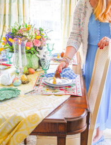 Katherine in blue spring dress and tweed cardigan places gingham napkin on table setting