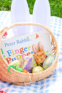 Vintage wicker bunny filled with a board book, sugar cookies, eggs, and bunny ears for a toddler Easter basket inspiration.