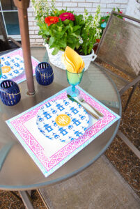 colorful summer decorating idea - patio table set with pink and blue Indian block print placemats, monogrammed pagoda plates, and zinnias