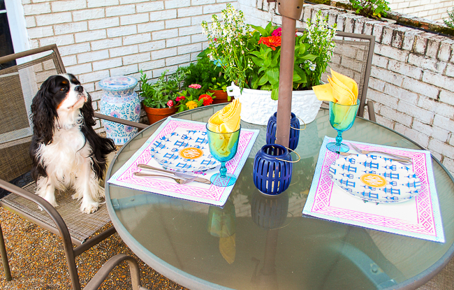 Patio tablescape with colorful placemats, pagoda monogrammed plates, and Henry sitting in chair