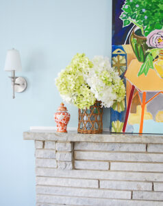 Bright mantel with abstract painting, hydrangea arrangement, and brass candlesticks for summer decorating ideas