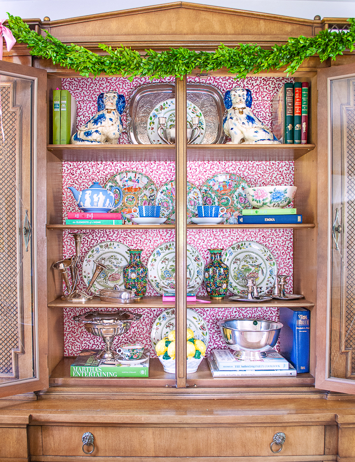 Updated china cabinet with wallpaper backing and shelves styled with vintage and antique tableware, dishes, decor, and silver