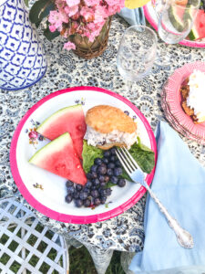 picnic table with plate full of summer fruit and chicken salad on croissant