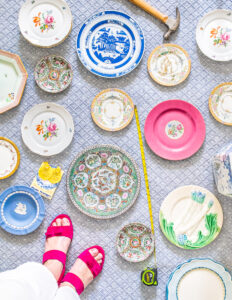 Top down perspective of varied vintage plates laid out on rug with hammer, nails, and measuring tape. Great way to curate a plate wall display.