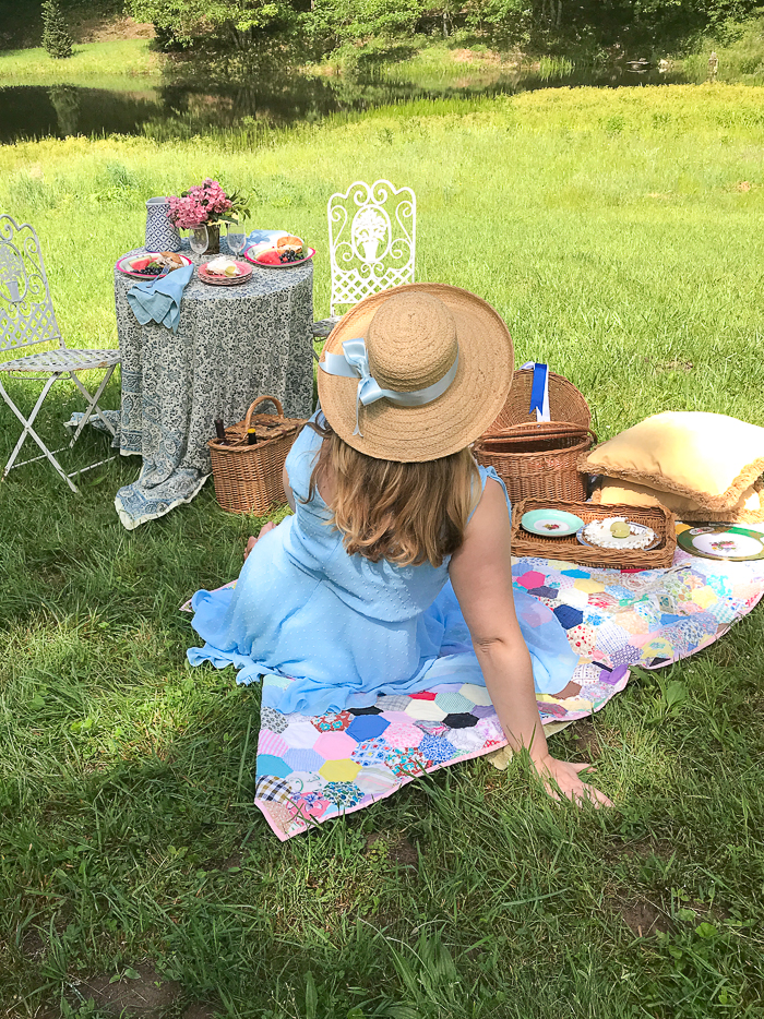 Katherine faces away sitting on picnic blanket with straw hat on and blue ribbon