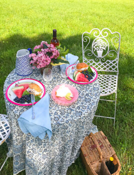 Picnic table set with vintage dishes, cloth napkins, and silver. Plates filled with chicken salad and fruit.