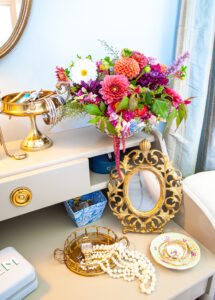 gilt table mirror with pearls arranged in tray and bowl of dahlias on shelf