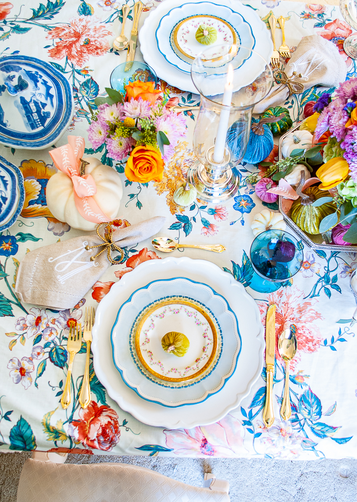 Top view of autumn tablescape with vintage chintz tablecloth, blue china, teal goblets, white pumpkins, blue and white willow dishes, and monogrammed napkins.