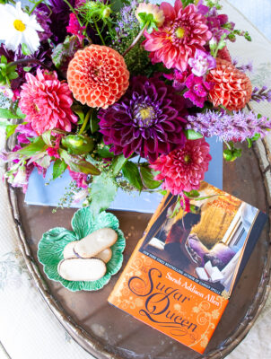 Sugar Queen book by Sarah Addison Allen on brass tray with dahlia floral arrangement and cookies