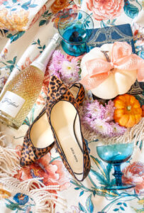 Fall inspiration collage flatlay with floral chintz background, pumpkins, pink mums, teal goblets, leopard print shoes, and champagne