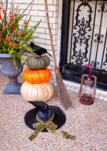 Witches hat, broom, and lantern beside heirloom pumpkin stack with crow give my front door a Halloween vibe