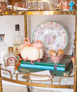 On bottom of bar cart white pumpkin with pink bow and antique floral plate