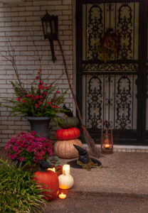 Candle light glows at this front door at dusk. Decorate for Halloween this year with a witchy front door by adding a witches hat, broom, and lantern to your autumn decor