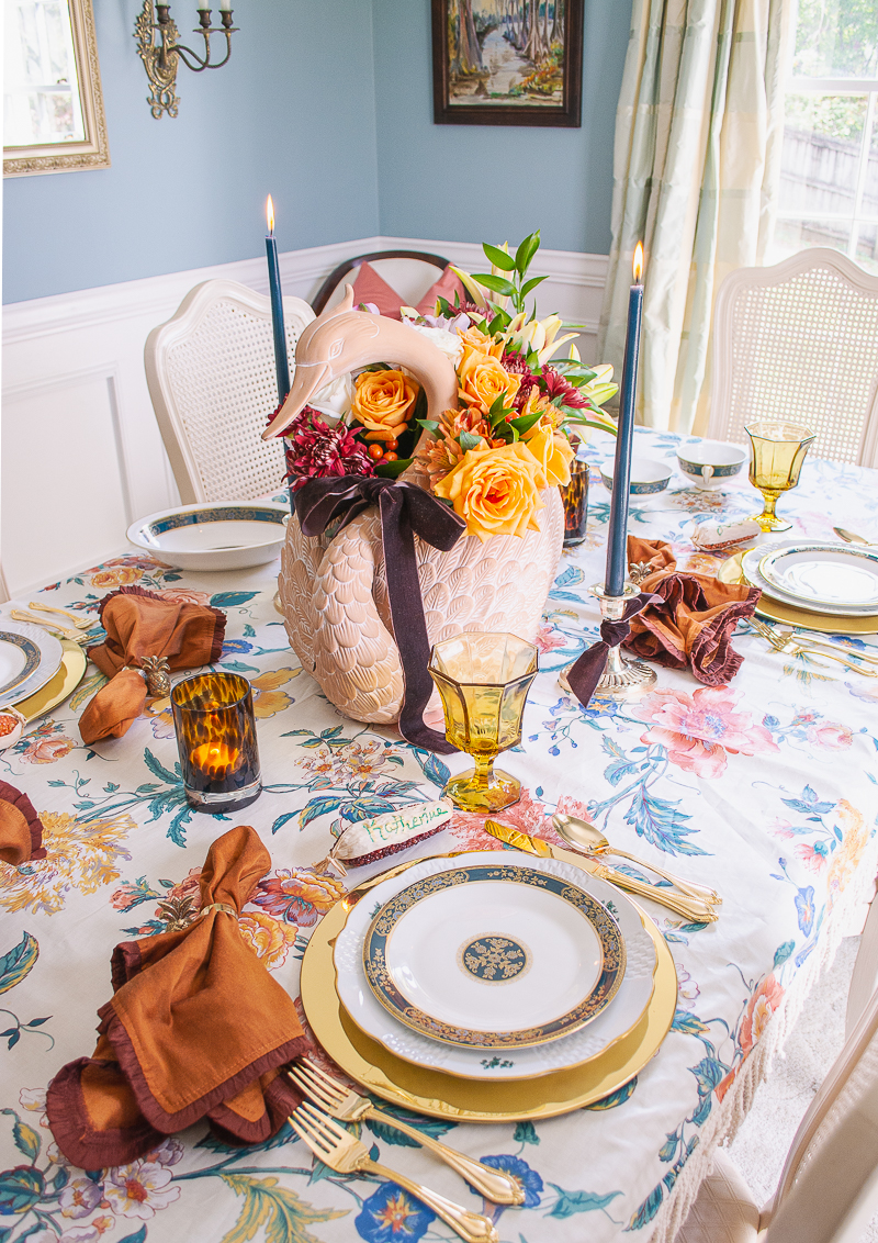 Elegant swan centerpiece with brown velvet bow, orange and white roses, burgundy mums, and lilies add drama to this Thanksgiving tablescape
