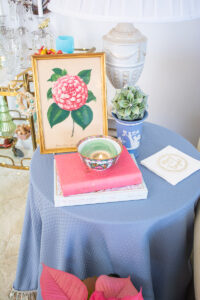 Blue skirted side table with books and candle, Wedgwood vase, and pink camellia print