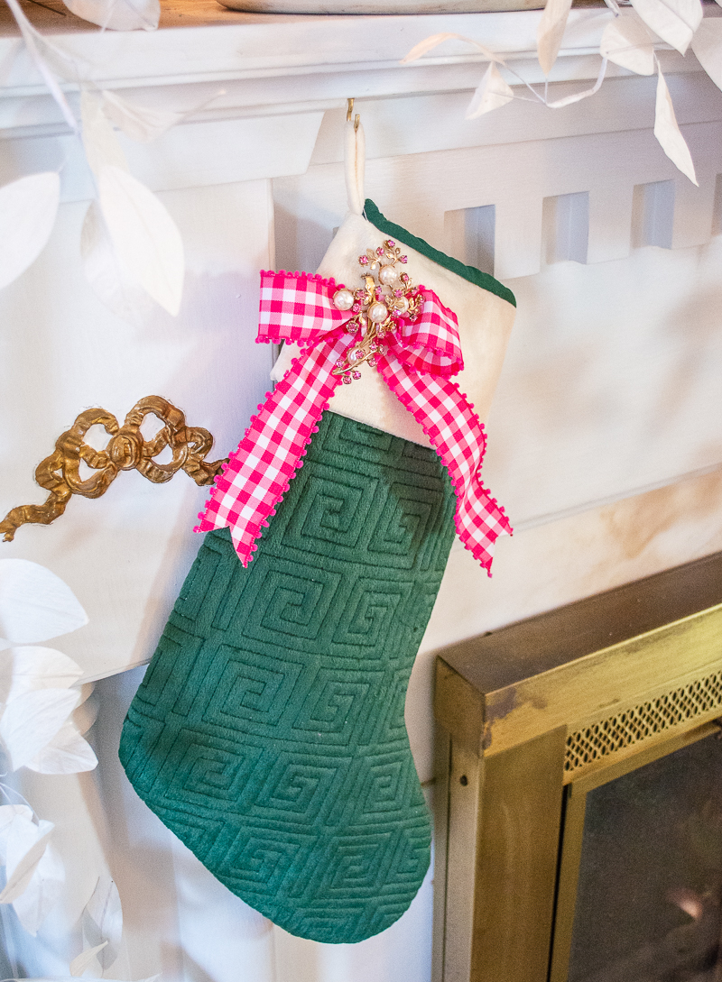 An emerald green Greek key stocking decorated with pink gingham ribbon and vintage brooch