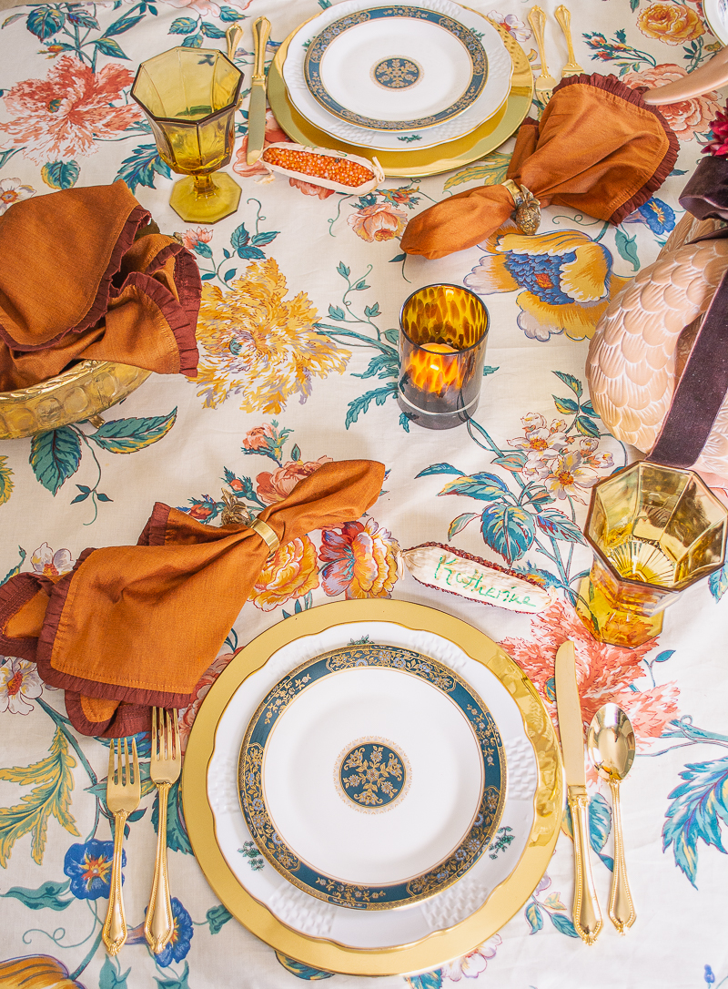 An intimate and chic Thanksgiving table set with chintz tablecloth, Royal Doulton Carlyle china, brown velvet, swan centerpiece, tortoise shell glass candles, and brass chargers