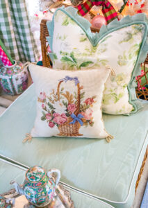 Floral basket needlepoint pillow on wicker day bed with green cushions