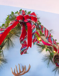 Plaid and red velvet multi-loop bow decorates the peak of the pine and ivy garland swags