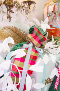 pink and green plaid ribbon with white paper branches and glitter feathers form a festive display on the mantel board