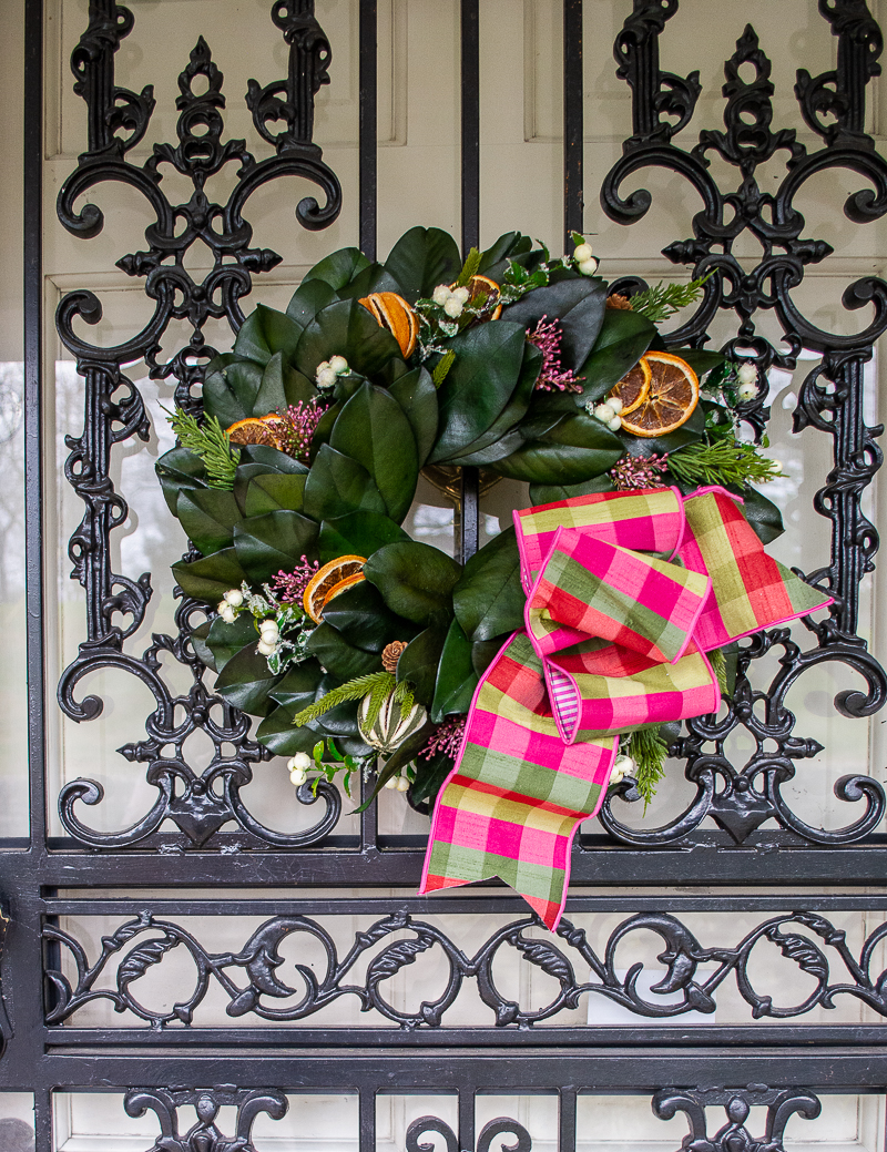 Williamsburg inspired magnolia & citrus wreath with pink and green gingham bow hung on wrought iron front door