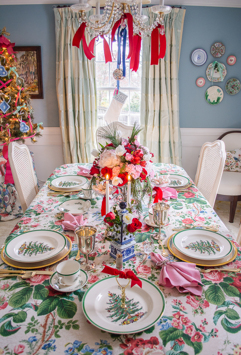 A grandmillennial Christmas table with vintage chintz tablecloth, heirloom silver, Spode Christmas tree china, and rose, peony floral centerpiece