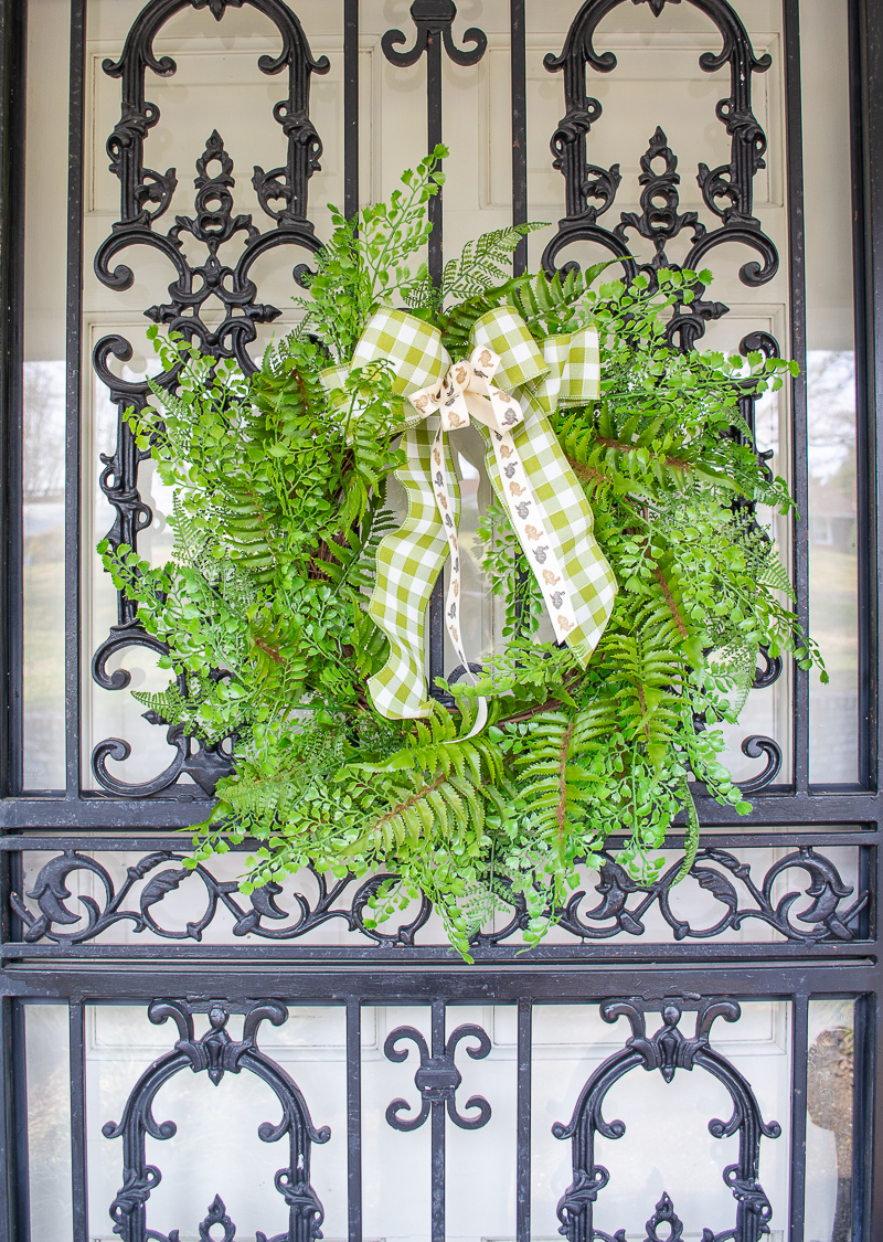 Add a little touch of spring with a faux fern wreath on black wrought iron front door with gingham and bunny ribbon bow