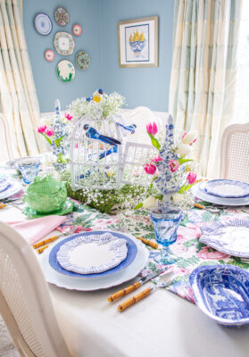 White wicker bird cage decorated with blue songbirds and baby's breath creates a whimsical spring centerpiece on this tablescape