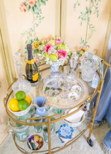 Top view of vintage bar cart decor including silver tray, coupes, fresh flowers, crystal ice bucket, and champagne
