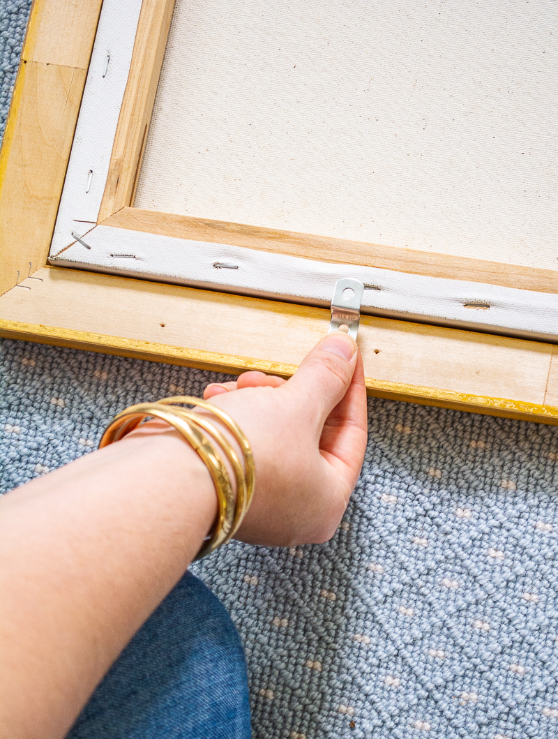 How to frame a painting with offset clips and a back-loading frame: here Katherine places a clip at the bottom of the painting and frame.