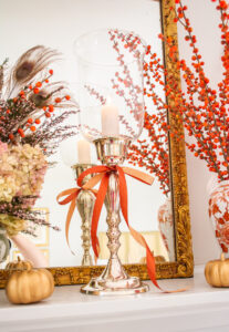 Silverplate candlestick with glass hurricane tied with orange bow on fall mantel