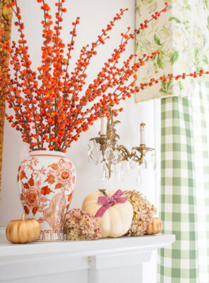 Small white pumpkin nestled in dried hydrangea blooms surrounding an orange and white Chinese vase filled with orange berry branches