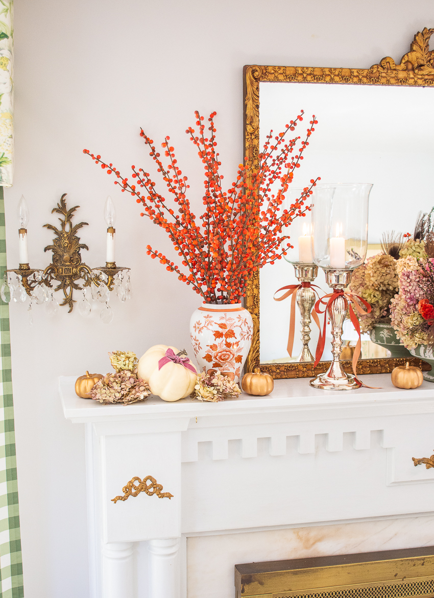 Branches of orange berries fill a Chinese orange and white vase surrounded by white pumpkins and preserved hydrangea blooms