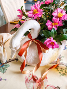 detail view of white swan planter filled with pink camellias and tied with satin bow