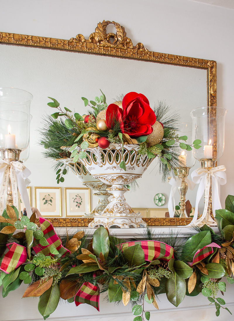 Grandmillennial Southern Christmas decor on mantel with white and gold compote filled with gold ornaments and red velvet magnolia bloom