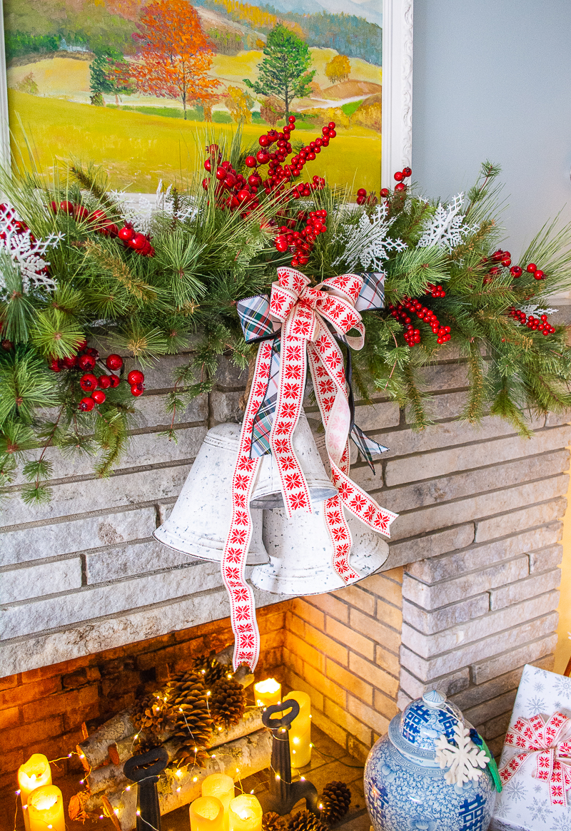 Lodge style mantel with red snowflake ribbon, white bells, pine garland, and red berries