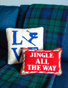 Après ski themed pillows on plaid blanket, including "Jingle all the way" needlepoint