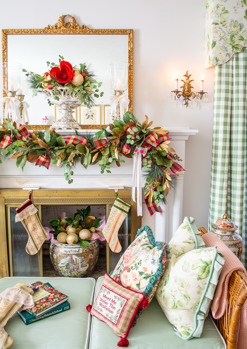 Front view of Grandmillennial Southern Christmas mantel decorated with magnolia and pine garland, pink and green plaid ribbon, vintage stockings, compote filled with magnolia