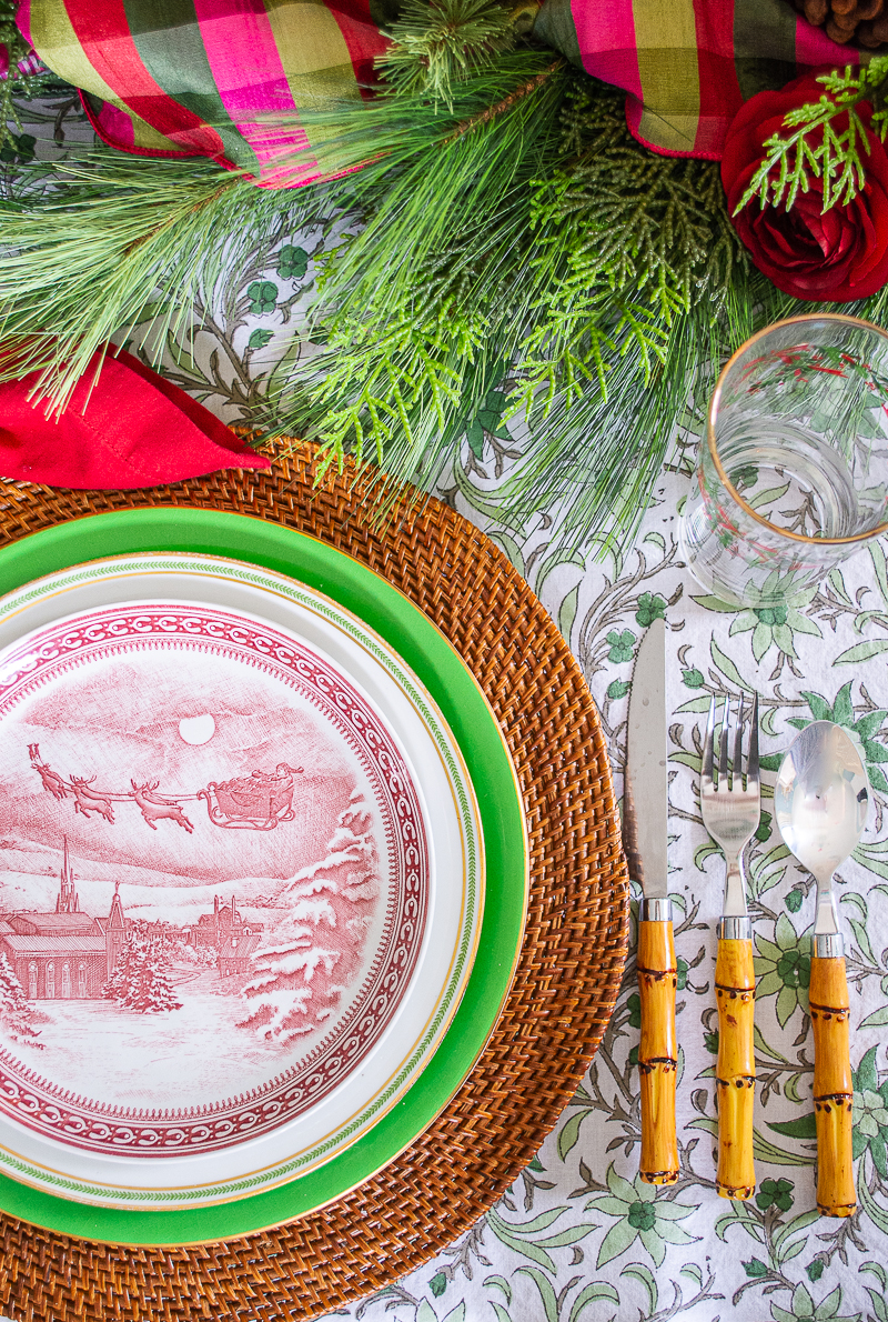 Detail view of place setting with Spode Santa plates, rattan charger, pine garland, and bamboo flatware