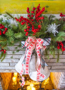 detail of snowflake ribbon bow and white bells hanging from faux pine swag on mantel