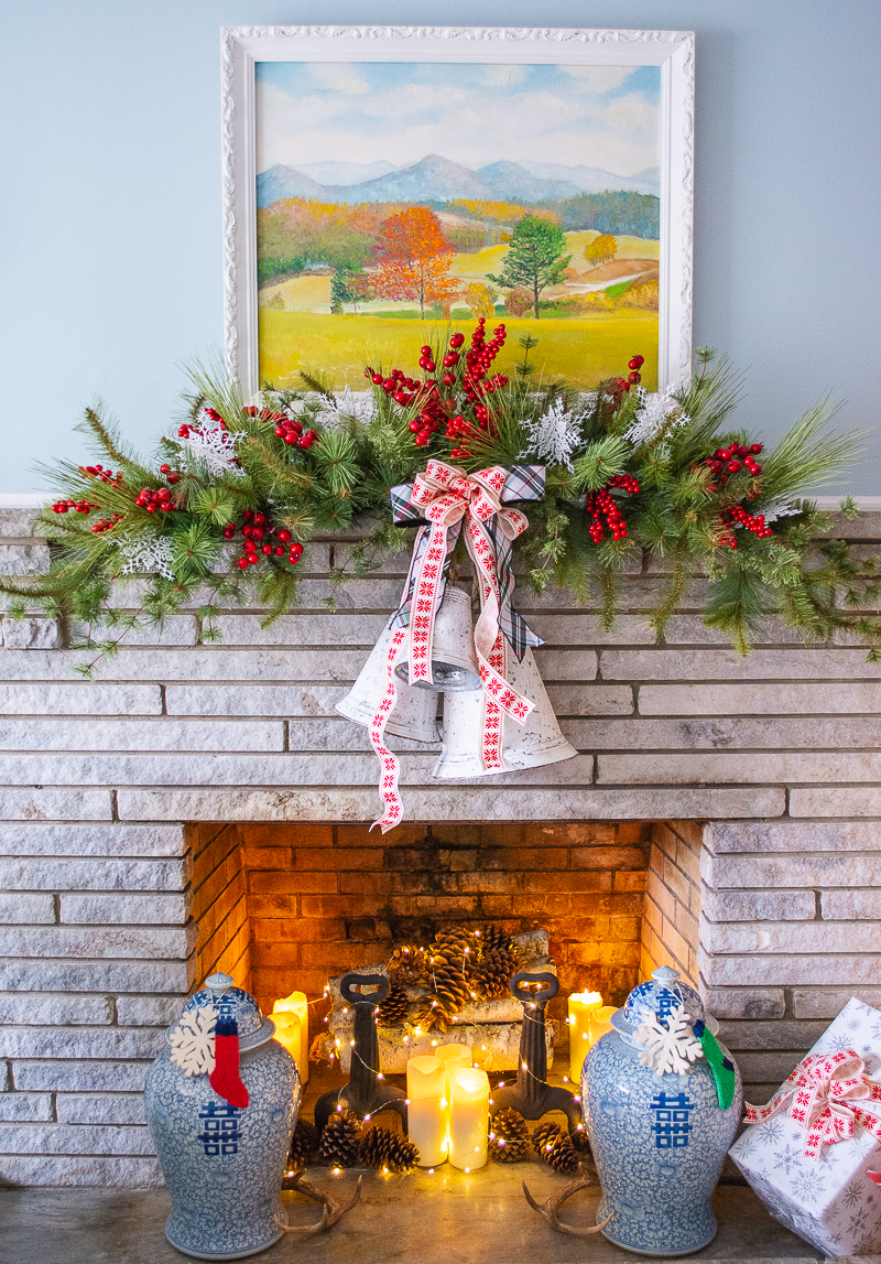 A cozy Christmas mantel with faux pine swags, red berries, white bells, and snowflake ribbon