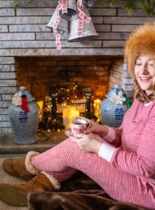 Katherine drinking cider in front of cozy Christmas mantel