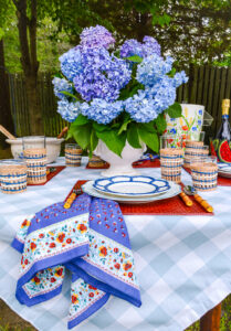 Summer tablescape for dining al fresco in red, white, and blue with gingham tablecloth, hydrangea centerpiece, and blue dishes